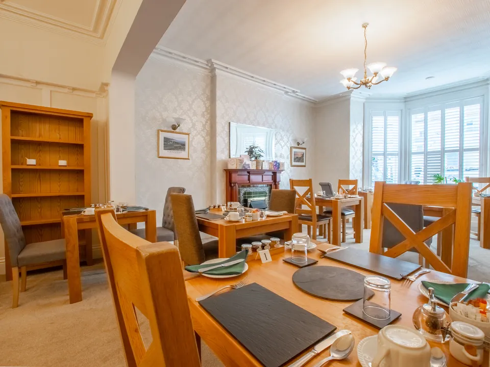 The breakfast room, with oak tables laid for breakfast and a bay window with shutters