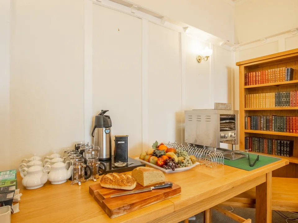 Fresh bread, fruit and tea and coffee laid out on the help-yourself table, next to a bookcase