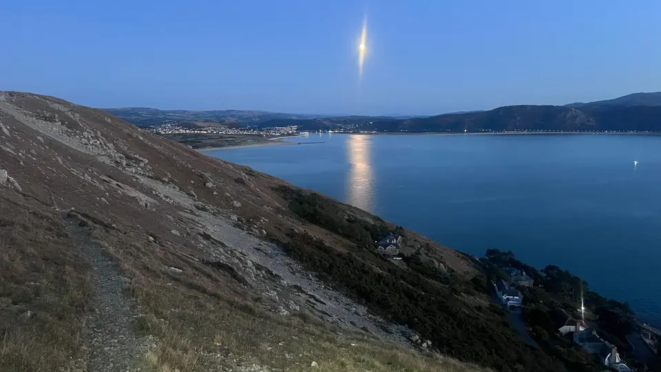 A path on the Orme at dusk, with the moon over the water and the hills beyond
