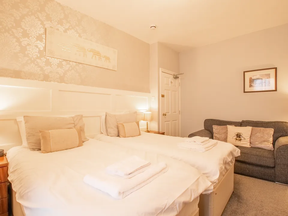 Beaumaris, Room 1: two single beds made up with white linen and towels, with a grey sofa by the door
