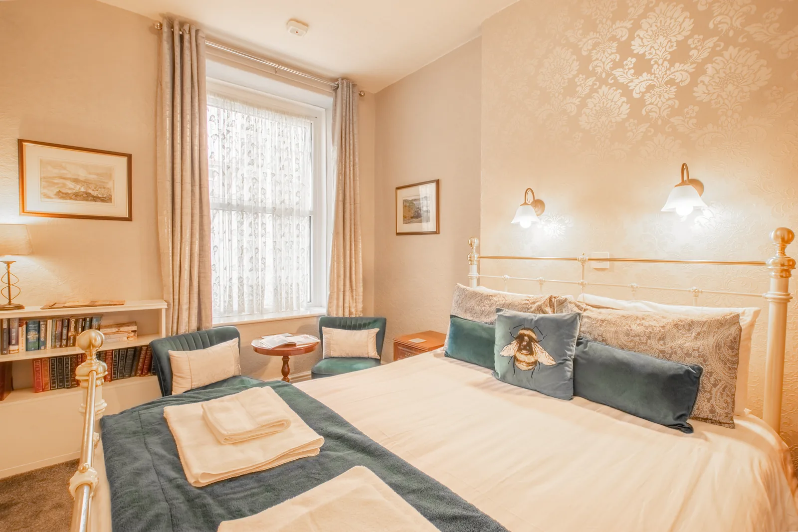 Penrhyn, Room 2: the bed made up with towels, with two teal armchairs by the window