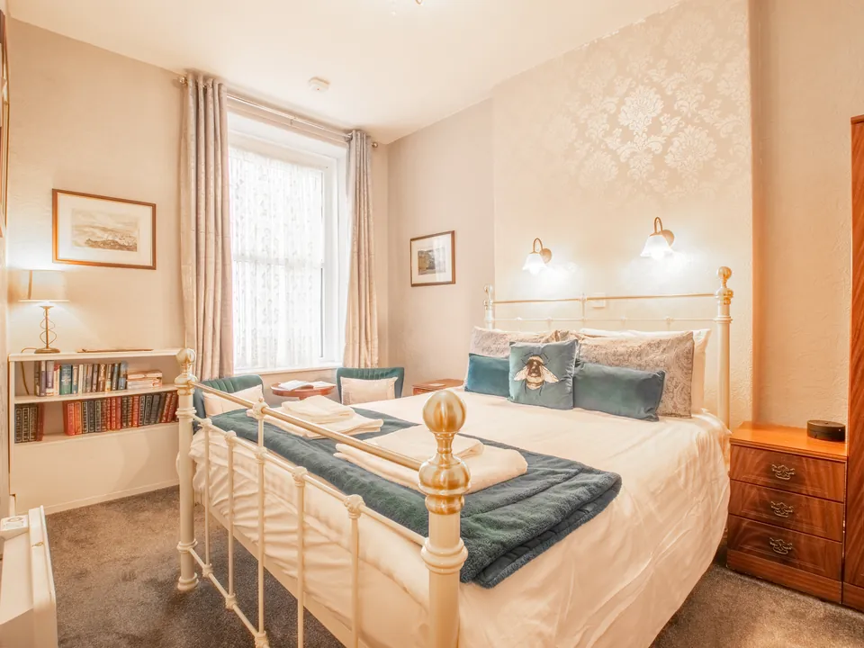 Penrhyn, Room 2: a cream and brass bed with teal cushions and throw, a bookshelf under the window and bedside lights