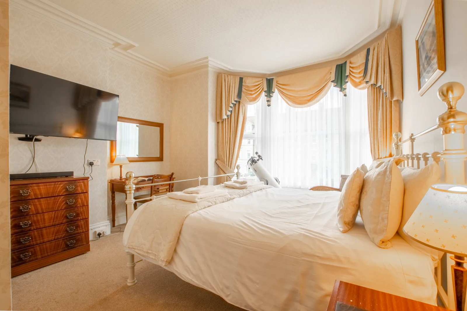 Adcote Suite, Room 3: the bed, a large wall-mounted TV, a chest of drawers and a dressing table in the bay