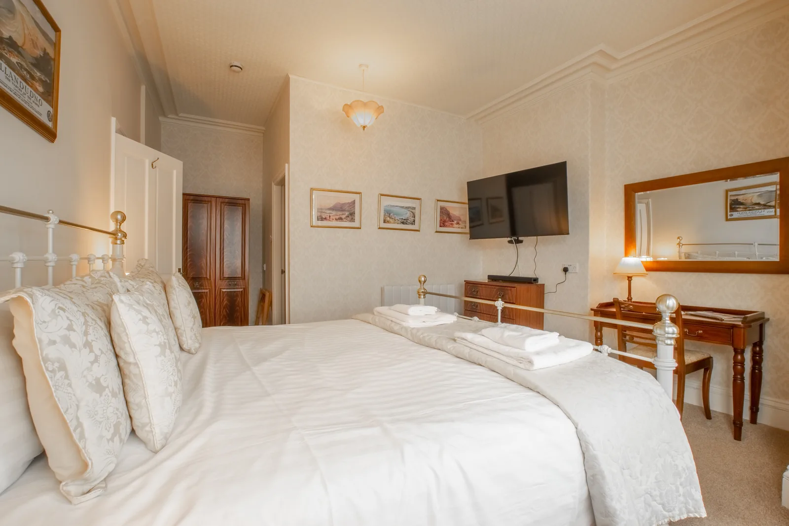 Adcote Suite, Room 3: the bed with cream pillows, a dressing table with a mirror, and pictures of the coast