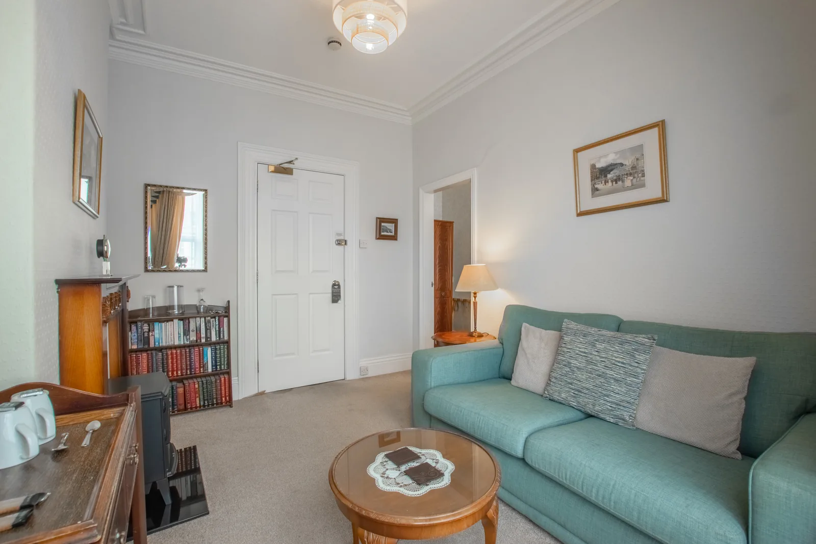 Adcote Suite, Room 3: the sitting room, with a teal sofa, a coffee table, a bookcase and the fire