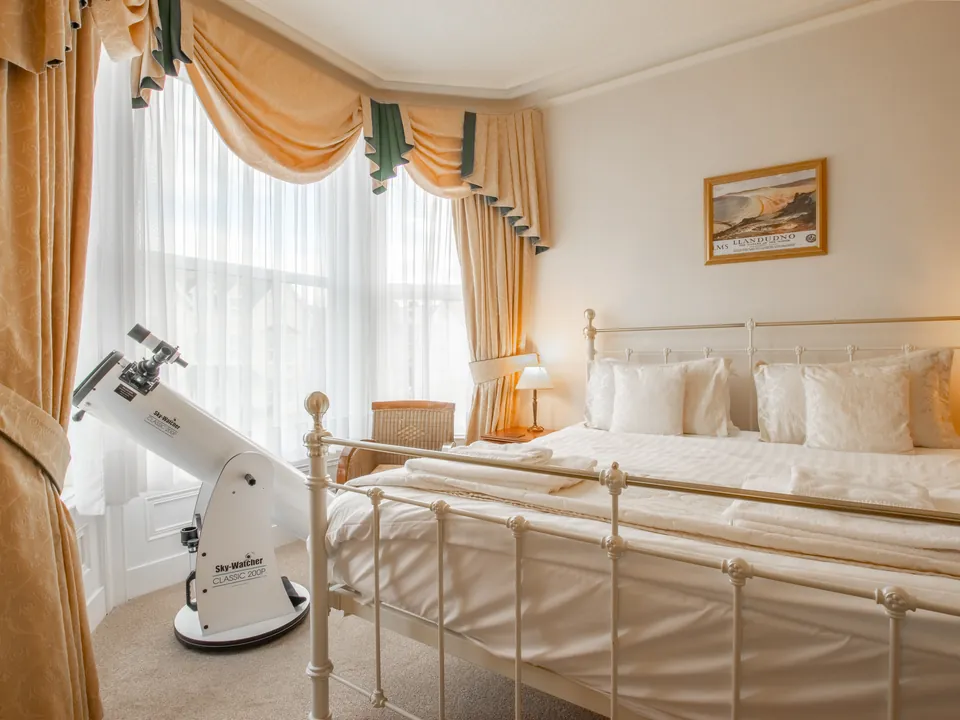 Adcote Suite, Room 3: a large brass bed in front of a bay window with swagged curtains, and a telescope by the window