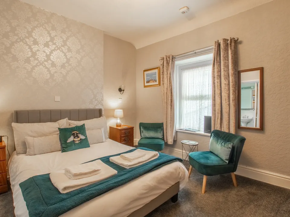 Caernarfon, Room 4: a double bed with a grey headboard and teal throw, and two teal velvet chairs by the window