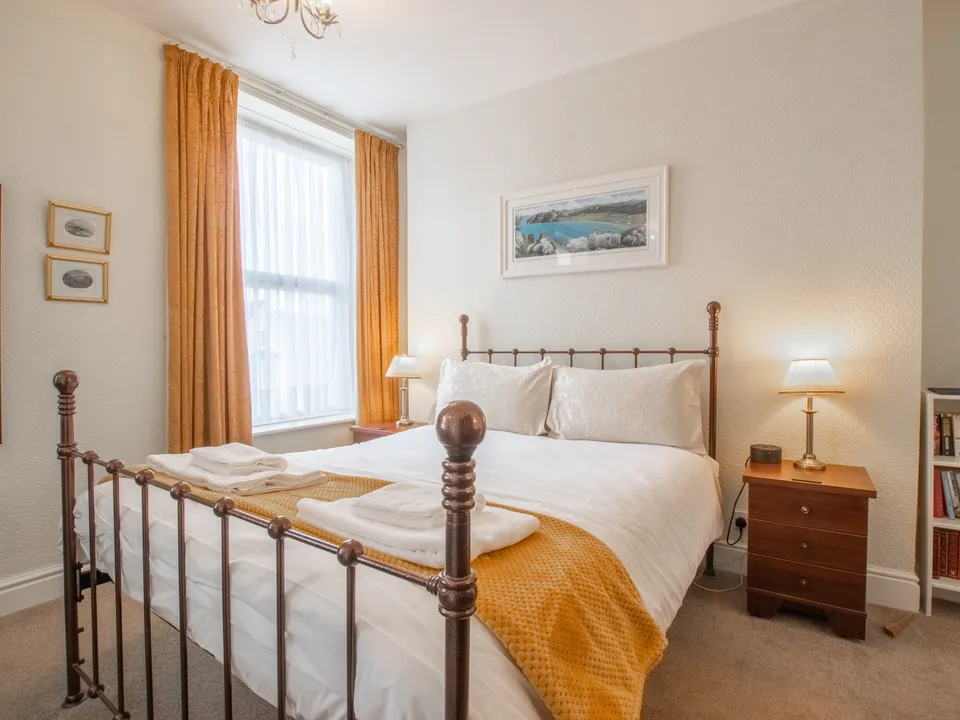 Conwy Studio, Room 6: a king size bed with a dark metal frame and a mustard throw, with tall windows and gold curtains