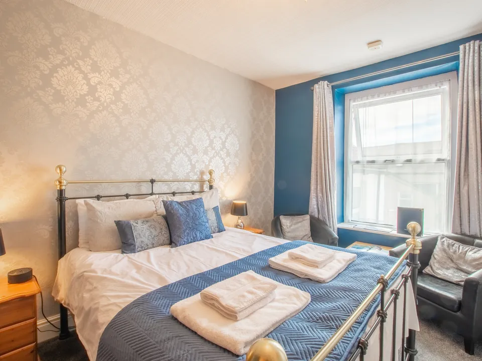 Harlech, Room 7: a brass bed with a blue throw and cushions, a blue feature wall and a leather armchair by the window